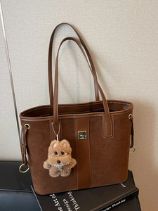 Large brown suede and leather tote bag with plush puppy charm on a design book