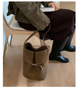Détail d'un sac seau en daim marron porté à l'épaule dans un décor minimaliste chic