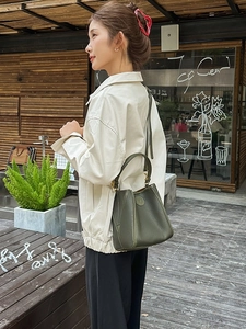 Dark green leather bucket bag with top handle and shoulder strap in street style setting