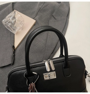 Détail d'un sac à main noir en cuir grainé avec ferrures argentées et breloque pompon cœur
