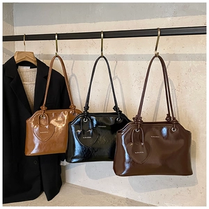 Trois cabas vintage en cuir brillant couleur caramel, noir et café suspendus au portant