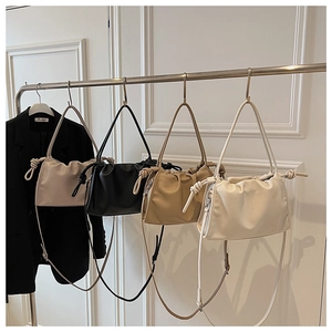 Row of pleated cloud bags in beige, black, and khaki hanging on a fashion display rack