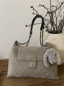 Schicke graue Stepptasche aus Wildleder mit Kettenriemen und Hasenanhänger auf Holztisch