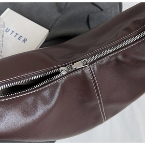 Détail du sac seau en cuir marron foncé avec fermeture éclair argentée et coutures blanches