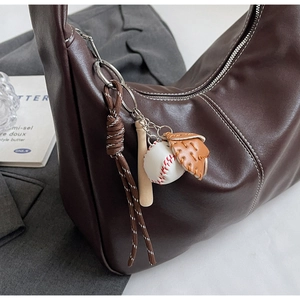 Gros plan sur le sac seau en cuir marron avec charme baseball et surpiqûres blanches