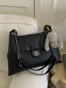 Schicke schwarze Stepptasche mit Kettenriemen und Plüschhasen-Anhänger auf dem Sofa