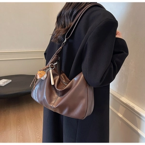 Détail du sac hobo en cuir marron foncé avec boucle argentée et pendentif de baseball