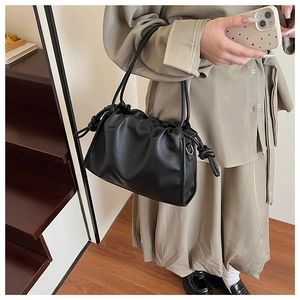 Detail of a black ruched leather cloud bag with drawstring and knot accents on model