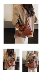 Détail du sac seau en cuir marron foncé avec coutures blanches et pompon décoratif
