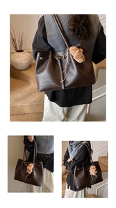 Macro shot of dark brown tote bag showing leather texture, buckles, and plush bear charm