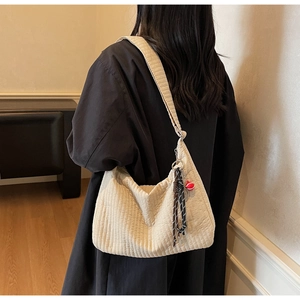 Close-up of beige corduroy hobo bag with tassel detail on a woman's shoulder