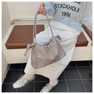Grey pleated cloud bag with knotted strap shown on model in a casual lifestyle setting