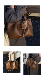 Detail of a large brown leather tote bag with a cute plush bear charm on shoulder