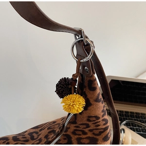 Close-up of leopard print shoulder bag with fur ball charms and leather strap detail