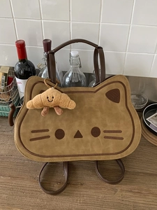 Cute cat-shaped brown suede backpack with croissant plush charm on a wooden table