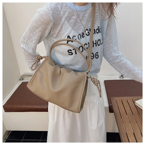 Close-up of khaki pleated leather cloud bag with knot details and handle worn by model