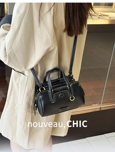 Street style view of a black Boston tote bag with white stitching and gold hardware