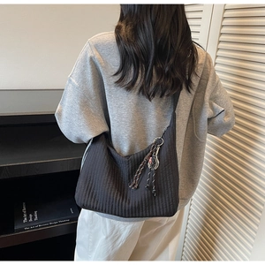 Detail of black quilted tote bag featuring creative tennis racket pendant and braided charm