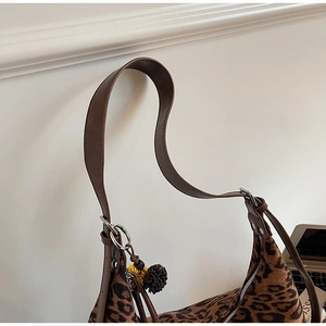 Detail of leopard print shoulder bag with brown leather strap and fuzzy pompom charm