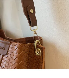 Dettaglio del gancio in metallo e logo impresso sulla borsa a secchiello marrone intrecciata