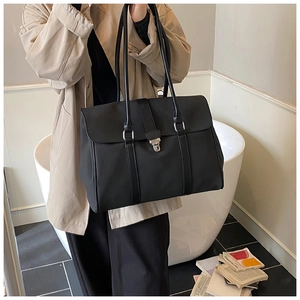 Dettaglio della borsa tote nera con manici in pelle indossata sulla spalla dalla modella