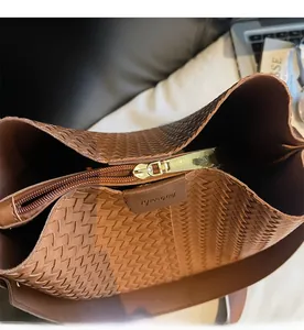 Dettaglio della cerniera dorata e della pelle intrecciata marrone della borsa a secchiello