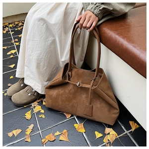 Detail view of large brown suede tote bag with metal buckle and long shoulder strap