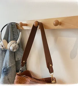 Dettaglio tracolla larga in pelle e fibbia dorata su borsa a mano intrecciata marrone
