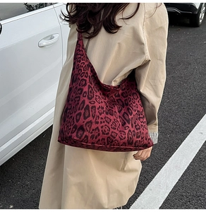 Close-up of a burgundy leopard print hobo bag worn with a beige trench coat for autumn