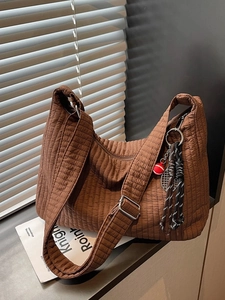 Large dark brown quilted tote bag with wide strap and charm shown in soft window light