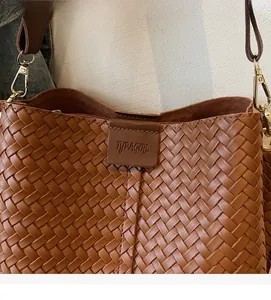 Dettaglio di borsa a secchiello intrecciata marrone con trama e etichetta in pelle goffrata
