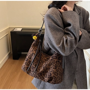 Detail view of leopard print shoulder bag with plush ball charm and slim leather strap