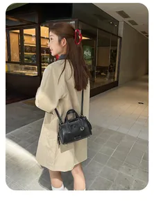 Side view of black Boston tote bag with white stitching shown on a model in a trench coat