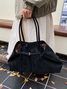 Chic black frosted suede tote bag with metal buckle on an autumn street background