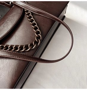 Detail of dark brown leather crossbody bag featuring vintage gold chain and glossy texture