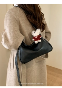 Close-up of minimalist black leather half-moon bag with cute white bear pendant