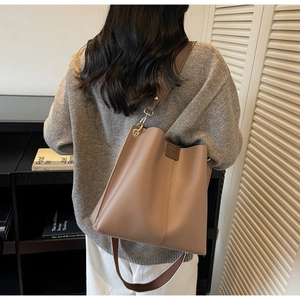 Dettaglio borsa a secchiello taupe con chiusura logo goffrata e tracolla larga su modella