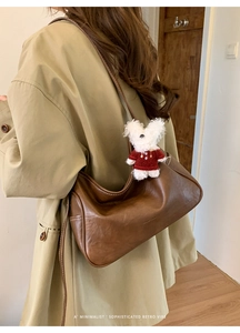 Brown retro leather hobo bag with a white plush bunny charm on a model side view