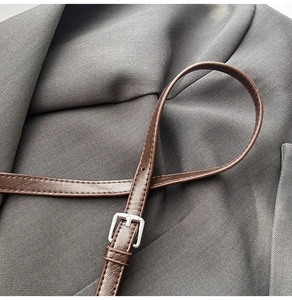 Close-up of brown leather shoulder strap with silver buckle on a dark blazer