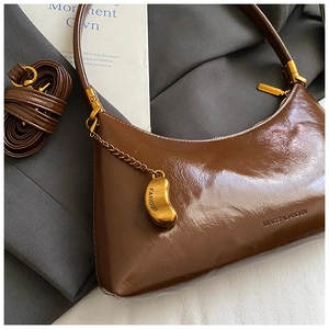Détail du sac hobo en similicuir marron brillant avec pendentif doré et bandoulière réglable