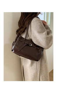 Dark brown leather tote bag with vintage buckle detail shown on a female model