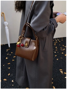 Detail view of a vintage dark brown bucket bag with golden lock and red cherry charm