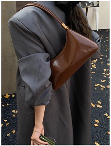 Détail d'un sac à bandoulière marron brillant avec finitions dorées et design chic
