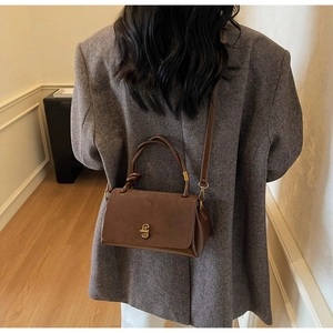 Detail of vintage brown suede crossbody bag with gold twist lock on grey tweed coat