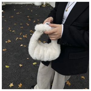 Détail d'un sac à main en peluche blanche avec poignée nouée sur fond de feuilles de ginkgo