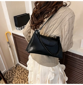 Chic black glossy leather baguette bag with chain detail worn over the shoulder