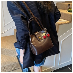 Detail of dark brown bucket bag with gold twist lock and red cherry charm accessory
