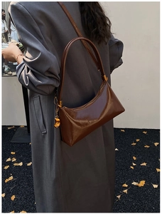 Détail d'un sac hobo en cuir brillant marron foncé avec un pendentif doré