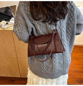 Detail of burgundy leather rectangular chain bag worn over a grey knit sweater