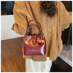 Close-up of wine red bucket bag with cherry pendant and golden clasp on a model
